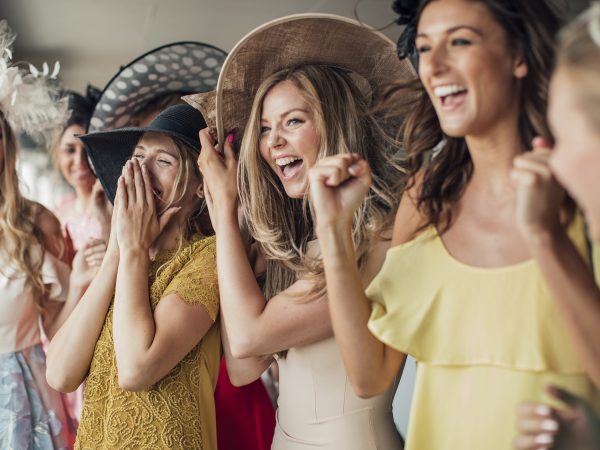 A group of young women cheering on for the running horses on ladies day.